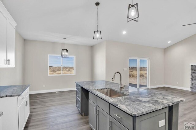 kitchen featuring pendant lighting, a kitchen island with sink, white cabinetry, a sink, and dark stone countertops