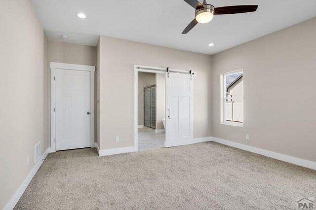 unfurnished bedroom featuring recessed lighting, light colored carpet, visible vents, a barn door, and baseboards