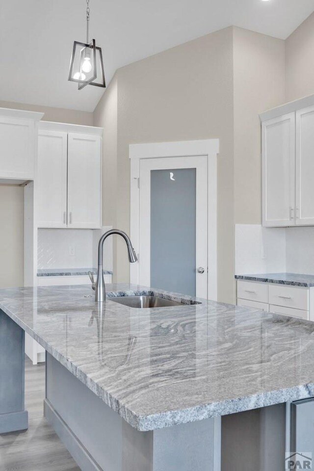 kitchen featuring white cabinets, light stone counters, a kitchen island with sink, pendant lighting, and a sink