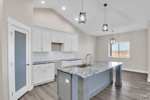 kitchen featuring an island with sink, a sink, white cabinetry, and decorative light fixtures