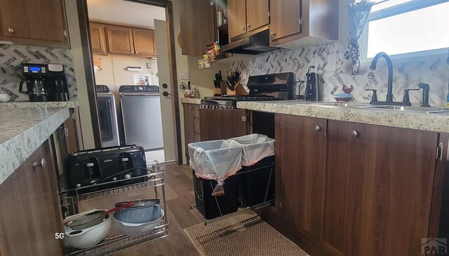 kitchen with washing machine and clothes dryer, light countertops, backsplash, a sink, and under cabinet range hood