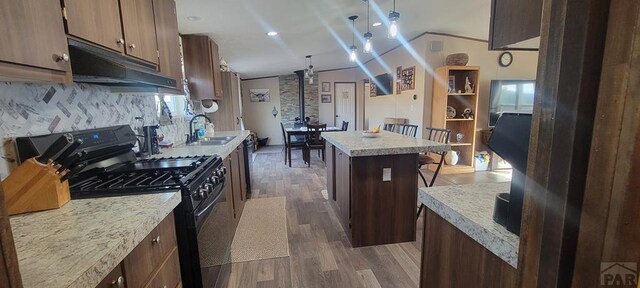 kitchen with a sink, a kitchen island, light countertops, a kitchen bar, and black gas range oven