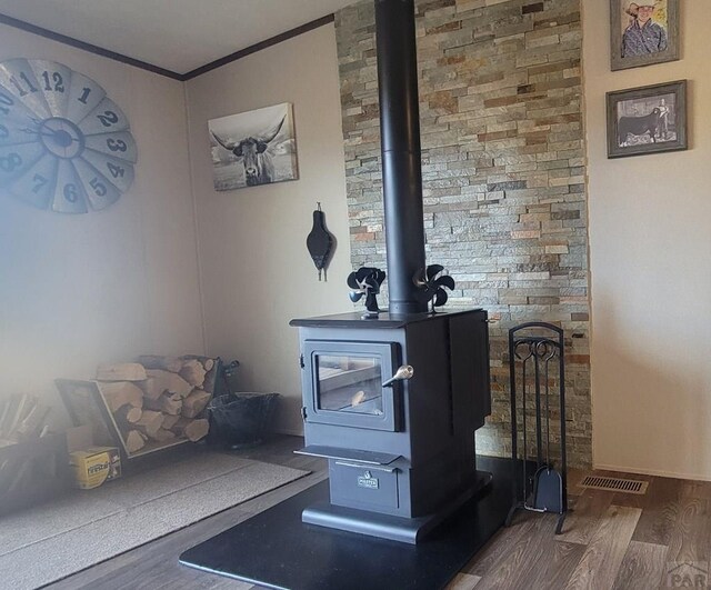 interior details featuring ornamental molding, a wood stove, visible vents, and wood finished floors