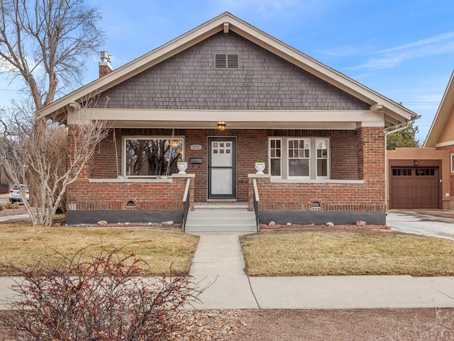 view of front facade with driveway, covered porch, a front lawn, and brick siding