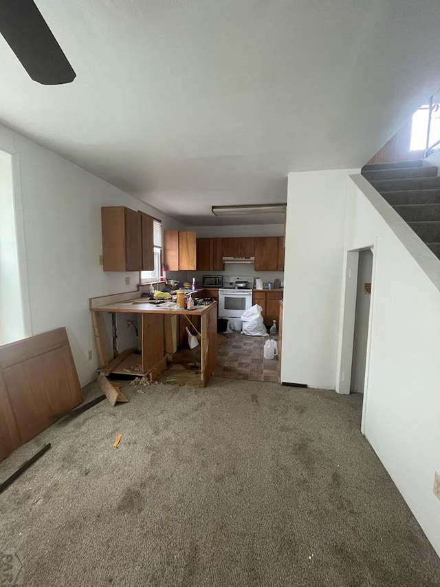 kitchen featuring carpet, brown cabinets, a peninsula, range with electric cooktop, and under cabinet range hood