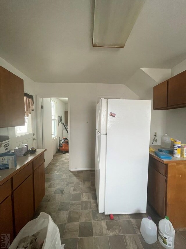 kitchen featuring lofted ceiling, brown cabinets, light countertops, and freestanding refrigerator