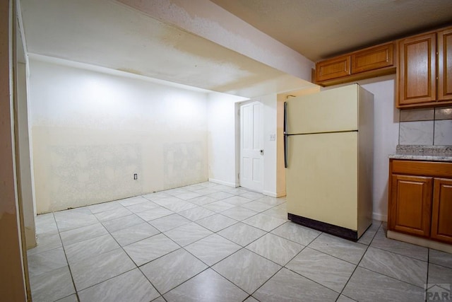 1142 Elm St, Pueblo, CO 81004 - kitchen featuring freestanding refrigerator, brown cabinets, and light tile patterned flooring