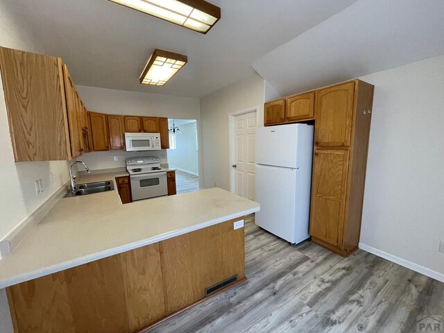 kitchen with white appliances, light wood-style flooring, a peninsula, light countertops, and a sink