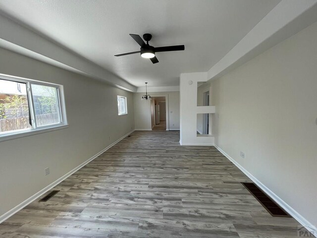 unfurnished living room featuring a healthy amount of sunlight, light wood finished floors, baseboards, and ceiling fan with notable chandelier