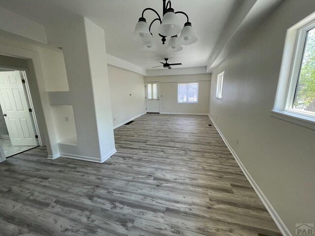 unfurnished living room featuring light wood-style floors, baseboards, a wealth of natural light, and ceiling fan with notable chandelier