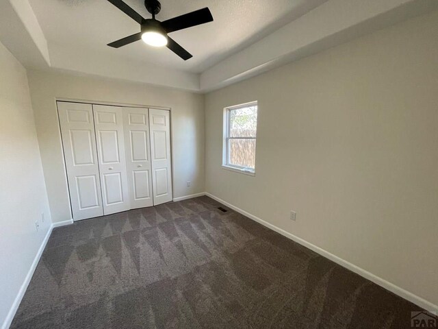 unfurnished bedroom featuring baseboards, dark colored carpet, a closet, and a raised ceiling