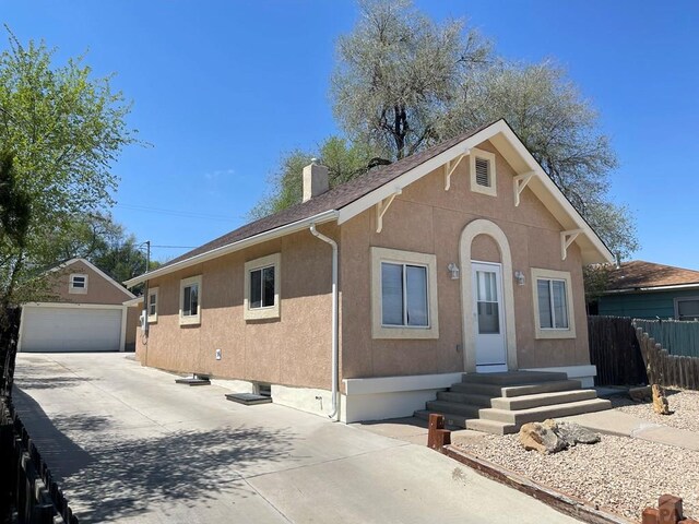 view of front facade featuring a garage, a chimney, an outbuilding, fence, and stucco siding