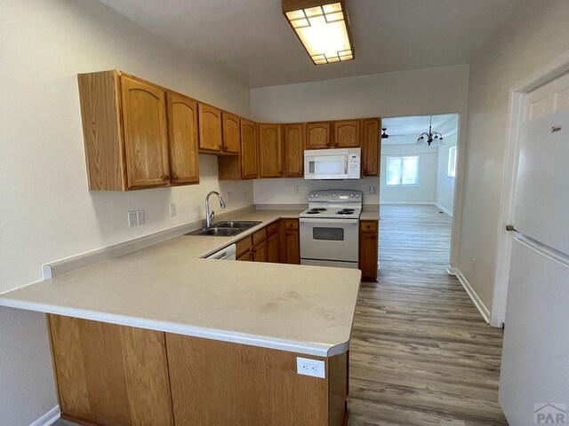 kitchen with a peninsula, white appliances, a sink, light countertops, and brown cabinetry