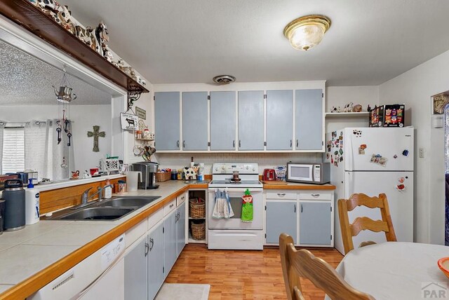 kitchen featuring tile counters, tasteful backsplash, light wood-style floors, a sink, and white appliances