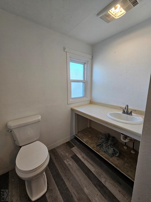 bathroom featuring toilet, wood finished floors, a sink, visible vents, and baseboards