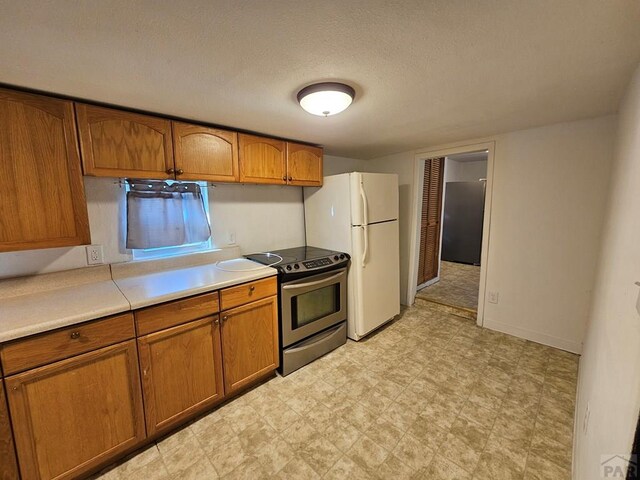 kitchen featuring light countertops, freestanding refrigerator, stainless steel electric range oven, light floors, and brown cabinetry