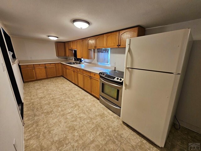 kitchen with electric stove, brown cabinets, freestanding refrigerator, light countertops, and light floors