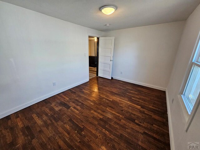 unfurnished room featuring dark wood-style flooring and baseboards