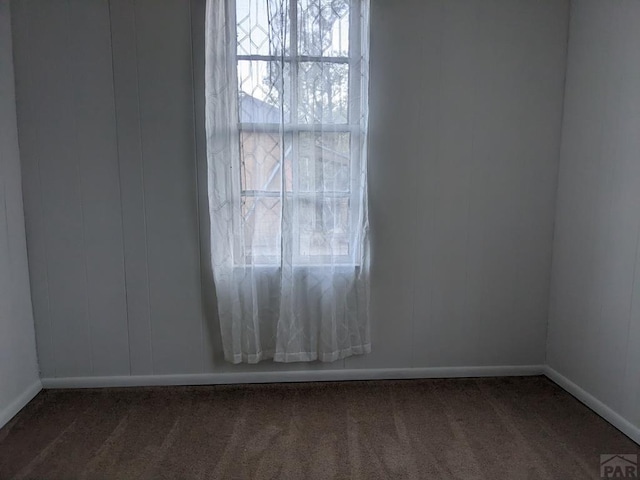 empty room featuring dark colored carpet and baseboards