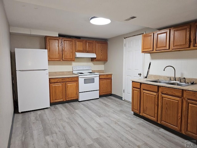 kitchen featuring under cabinet range hood, white appliances, a sink, light countertops, and brown cabinets