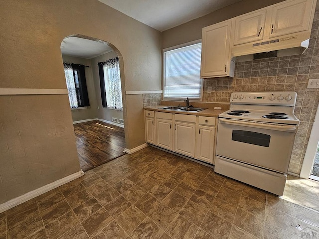 kitchen featuring arched walkways, electric stove, light countertops, under cabinet range hood, and a sink