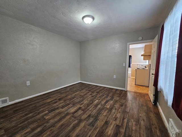 unfurnished room featuring baseboards, visible vents, a textured wall, dark wood-type flooring, and a textured ceiling