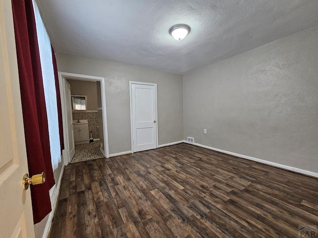 unfurnished bedroom with a textured ceiling, dark wood finished floors, visible vents, and baseboards