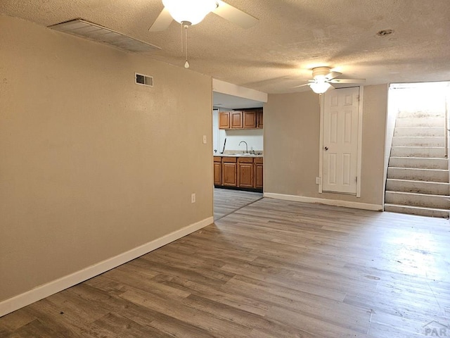 unfurnished living room featuring light wood finished floors, baseboards, visible vents, a ceiling fan, and a sink