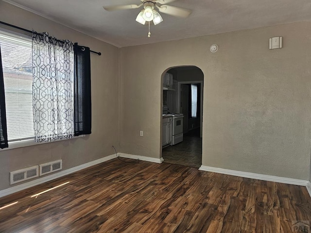 spare room with arched walkways, visible vents, baseboards, a ceiling fan, and dark wood-style floors