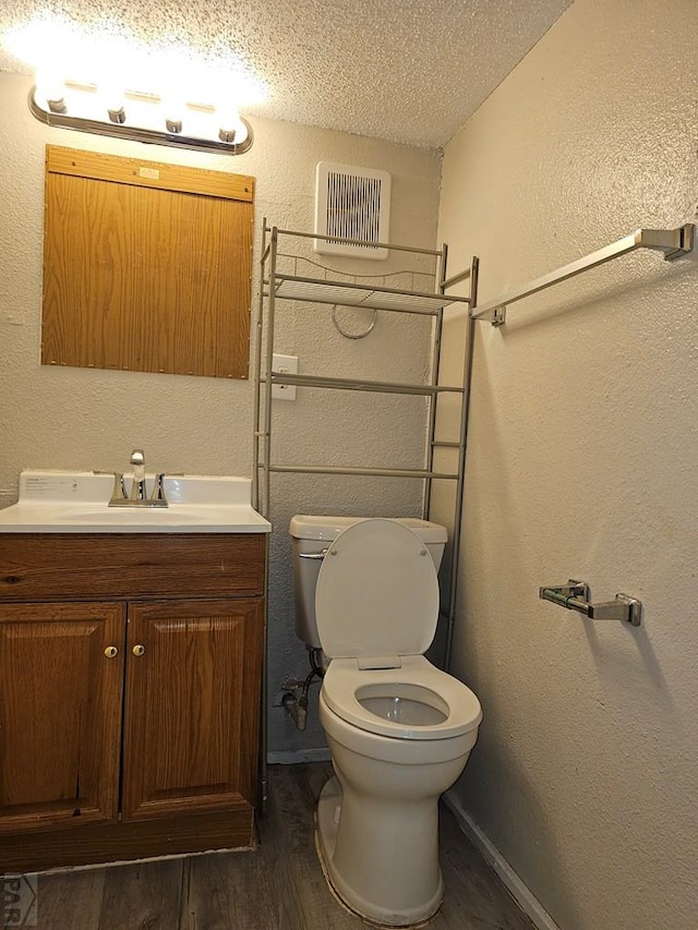 bathroom with a textured ceiling, a textured wall, wood finished floors, vanity, and visible vents