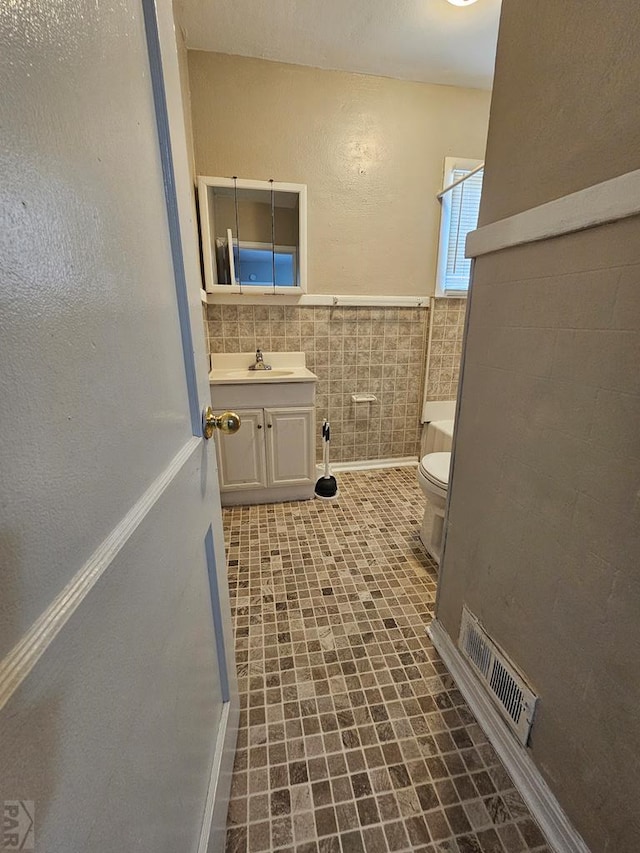 full bathroom with toilet, vanity, visible vents, tile walls, and wainscoting