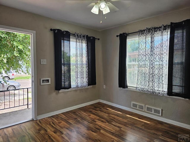 unfurnished room featuring dark wood-style floors, ceiling fan, visible vents, and baseboards