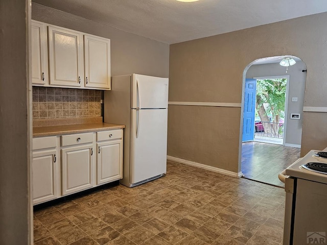 kitchen with arched walkways, white appliances, backsplash, and white cabinets