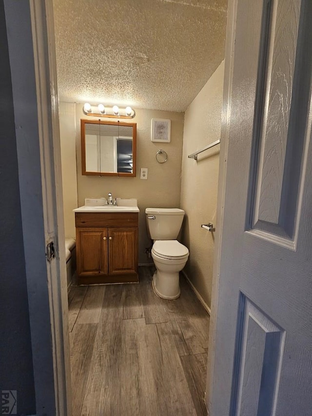 bathroom with a textured ceiling, toilet, wood finished floors, vanity, and baseboards