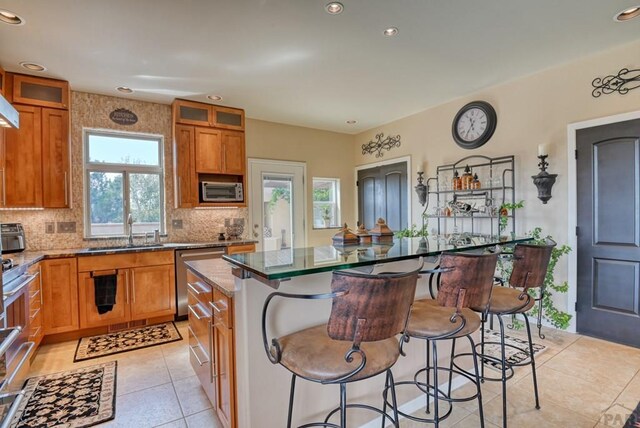 kitchen featuring a sink, a center island, a kitchen breakfast bar, brown cabinets, and glass insert cabinets