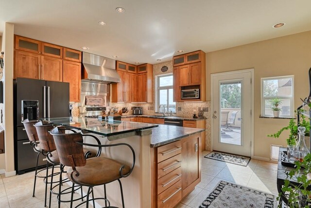 kitchen with a breakfast bar, glass insert cabinets, a kitchen island, black appliances, and wall chimney exhaust hood