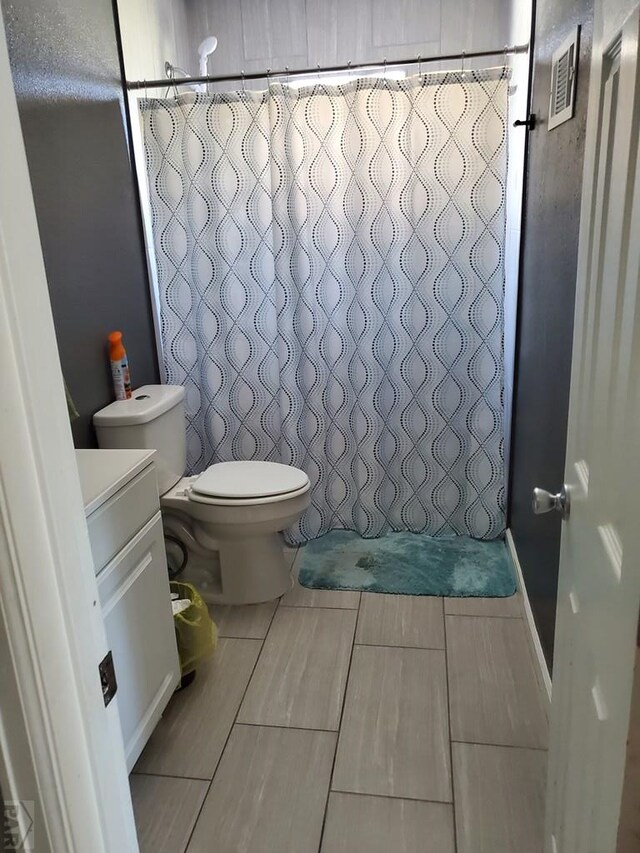 full bath with a tile shower, toilet, vanity, and visible vents