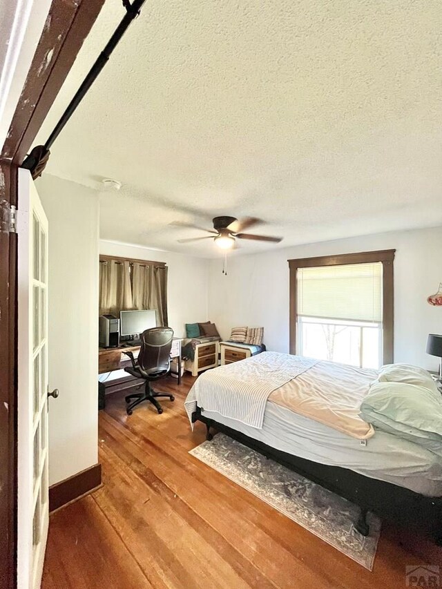 bedroom with a textured ceiling, a ceiling fan, and wood finished floors