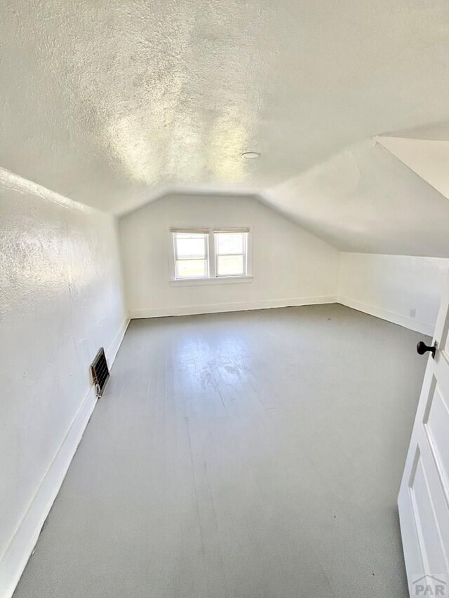 bonus room featuring a textured ceiling, lofted ceiling, and baseboards