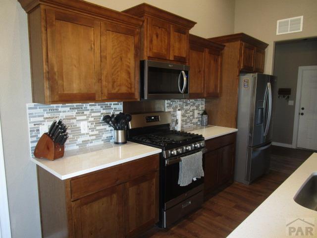 kitchen featuring tasteful backsplash, appliances with stainless steel finishes, visible vents, light countertops, and dark wood-type flooring