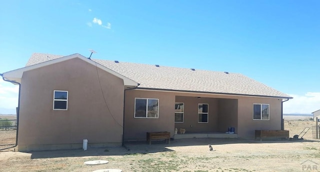 back of house featuring fence, a shingled roof, and stucco siding