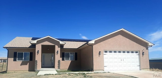 ranch-style house featuring stucco siding, solar panels, driveway, and an attached garage