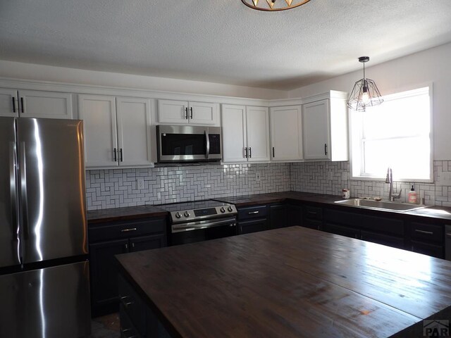 kitchen with a sink, appliances with stainless steel finishes, butcher block counters, and white cabinetry