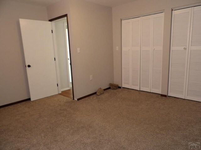 unfurnished bedroom featuring carpet floors, baseboards, and multiple closets