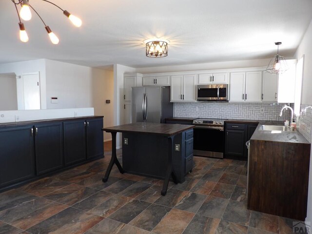 kitchen with a center island, decorative light fixtures, appliances with stainless steel finishes, white cabinetry, and a sink