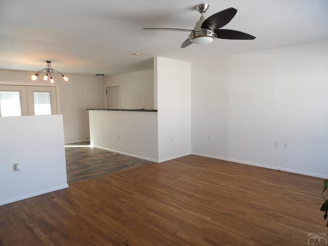 empty room featuring dark wood-type flooring, baseboards, and ceiling fan with notable chandelier