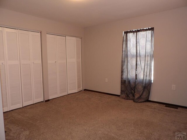 unfurnished bedroom featuring multiple closets and carpet flooring