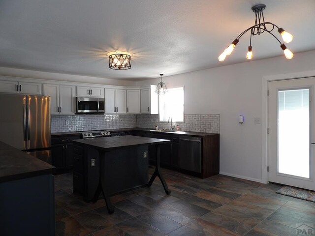 kitchen with pendant lighting, stainless steel appliances, dark countertops, decorative backsplash, and white cabinetry