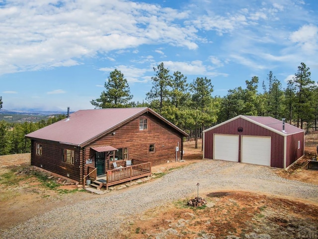 view of home's exterior with an outbuilding, a wooden deck, a detached garage, log siding, and gravel driveway
