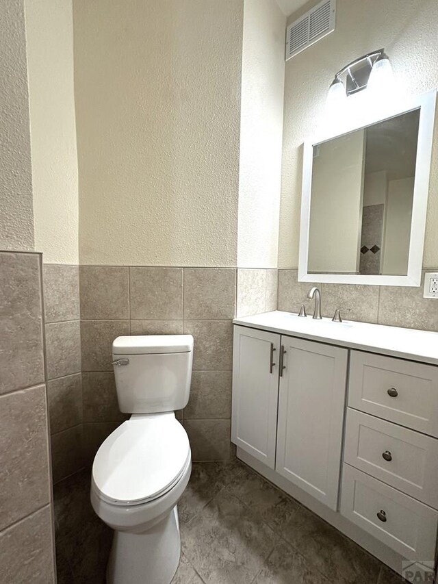 bathroom featuring tile walls, visible vents, a textured wall, toilet, and vanity